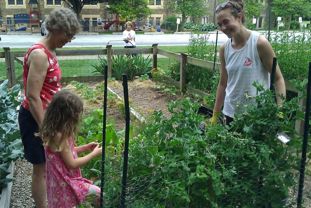Two older woman smiling looking at a young girl investigating a garden.