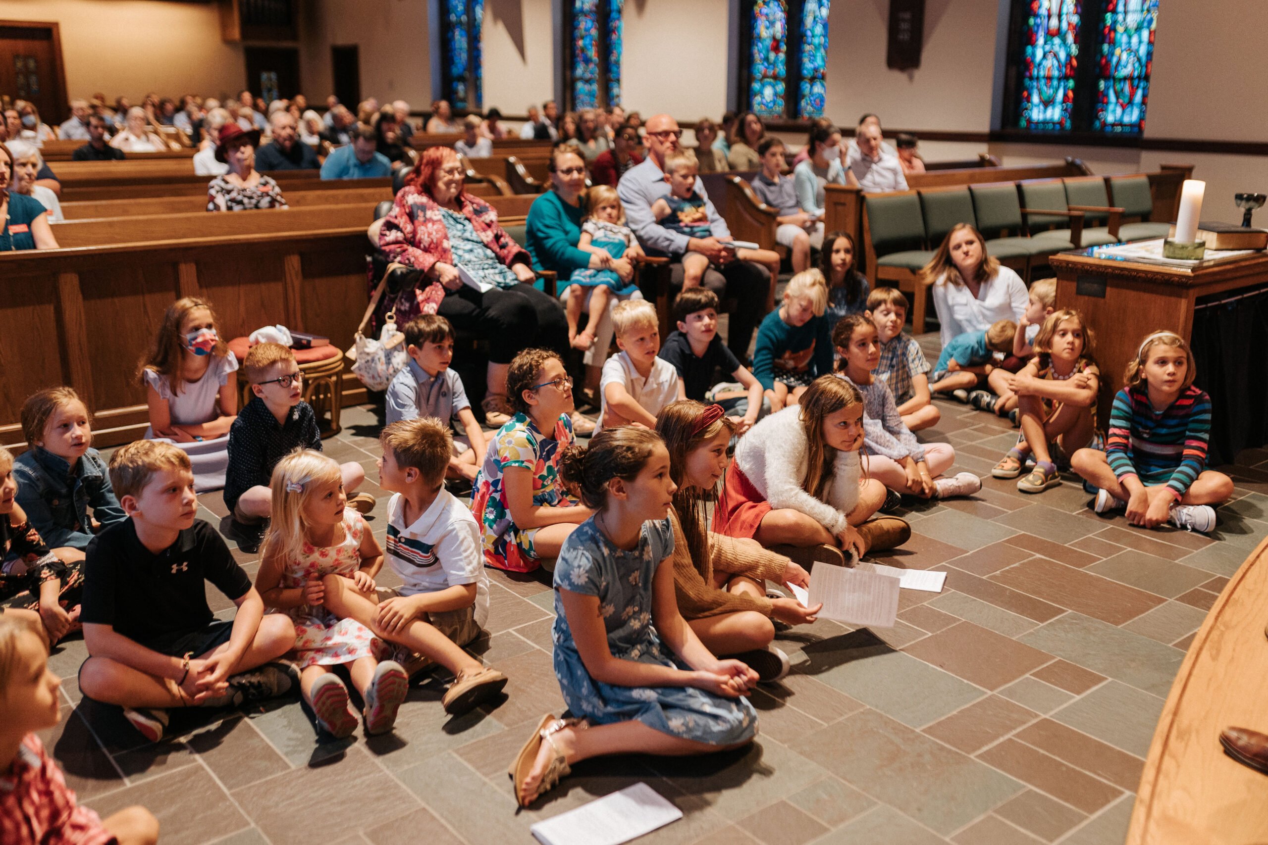 photo of young children sitting on the floor in the church looking towards the front of the church.